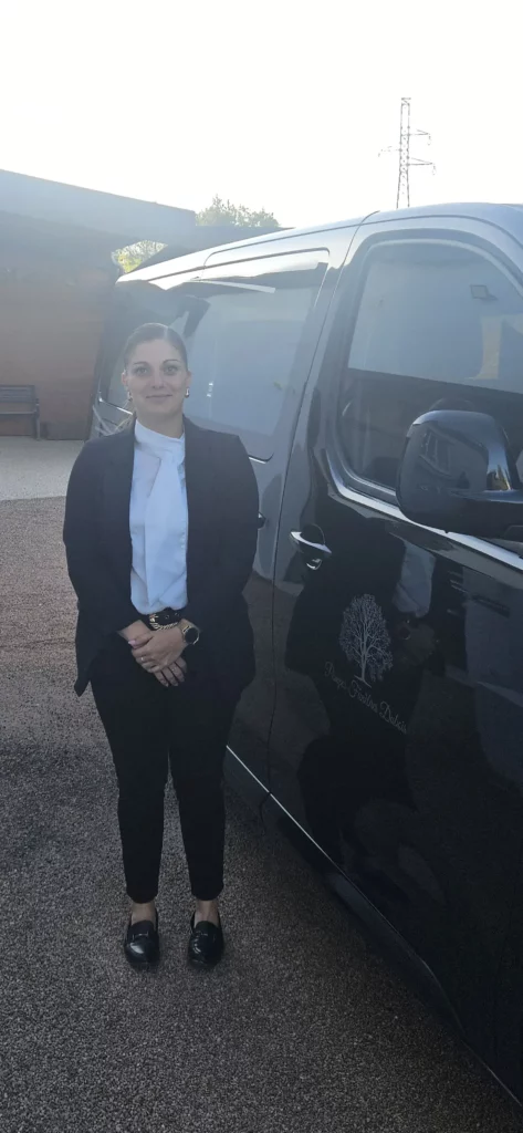 Conseillère funéraire en tenue professionnelle devant un véhicule funéraire Dubois.