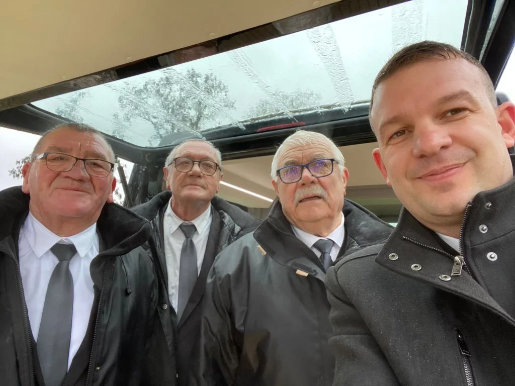 Équipe de quatre porteurs funéraires en selfie à l'arrière d'un véhicule.