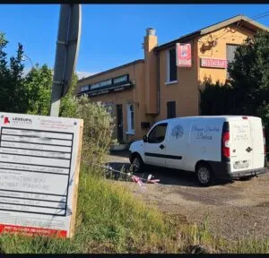 Fourgonnette des Pompes Funèbres Dubois stationnée devant un bâtiment avec un panneau de chantier.