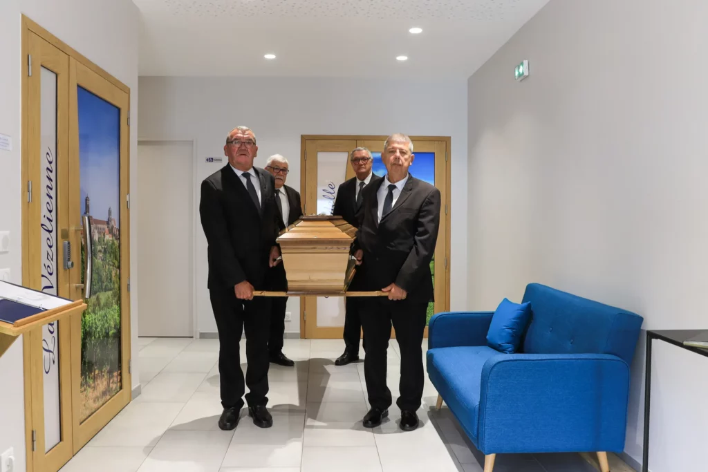 Quatre porteurs en costume transportant solennellement un cercueil.